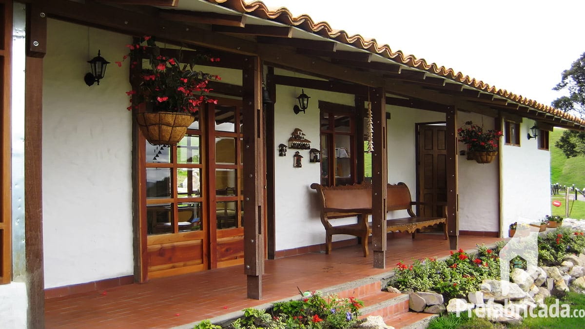 Detalle del porche de una casa prefabricada con vigas de madera, ventanal de madera y jardín interior