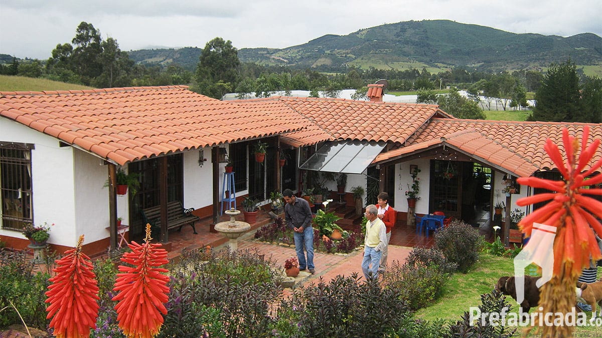 Conjunto de casas prefabricadas con teja de barro en fila, operarios en obra y montaña al fondo
