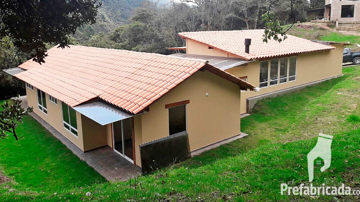 Casa prefabricada beige con teja, buhardilla, ventanal y jardín en pendiente