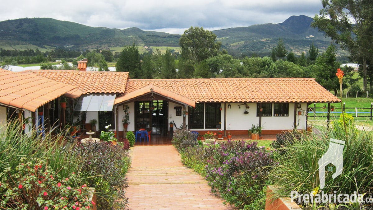 Casas prefabricadas con teja de barro, jardín con flores y camino de acceso, con montañas al fondo