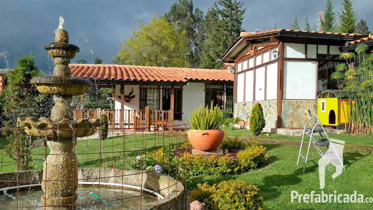Casa prefabricada campestre con teja de barro, fuente, pérgola y jardín con árboles