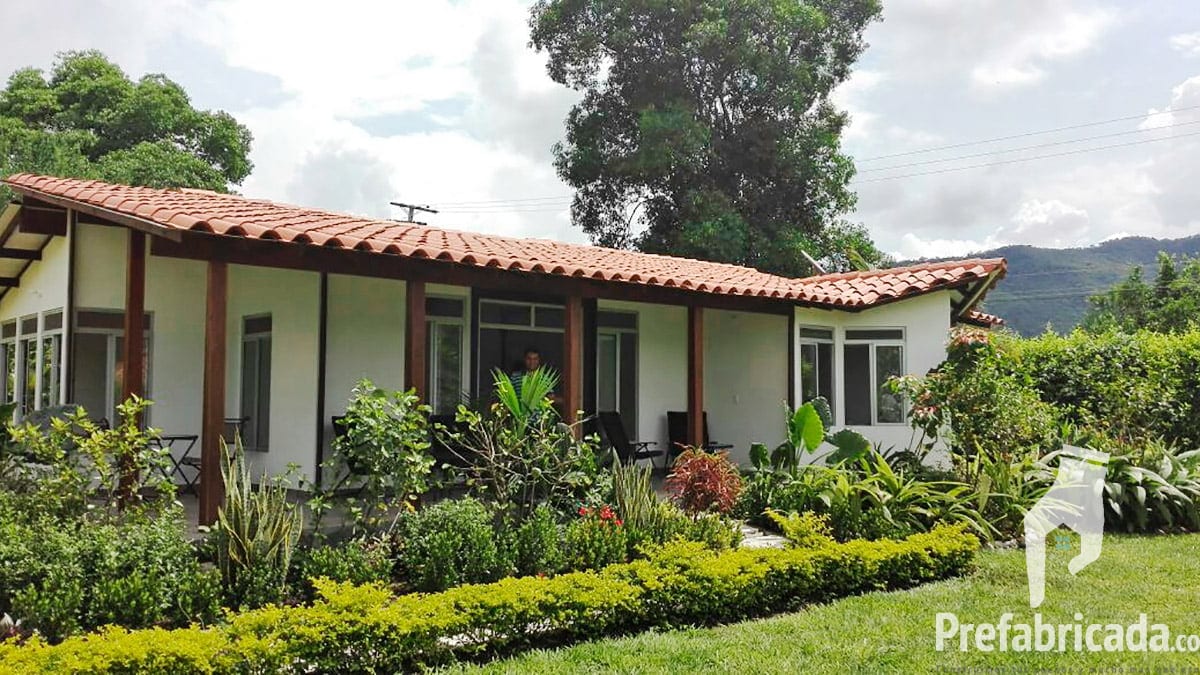 Casa prefabricada con teja de barro y jardín frondoso, con montañas Colombianas al fondo
