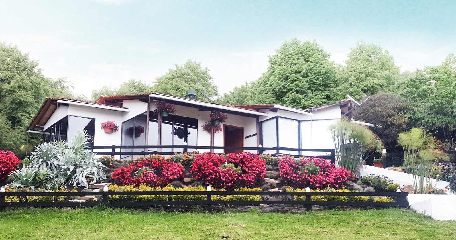Casa prefabricada blanca con porche, jardín con flores rosadas y colinas al fondo